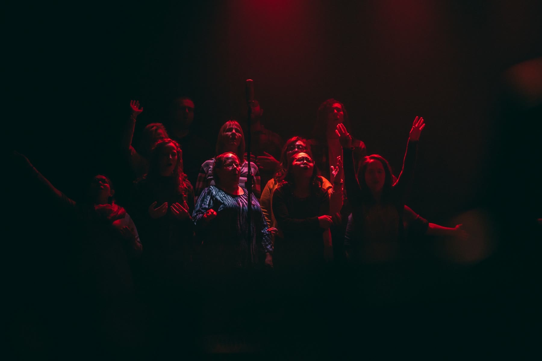 Gruppo di cantanti sul palco raccolto intorno a un microfono sotto luci rosse