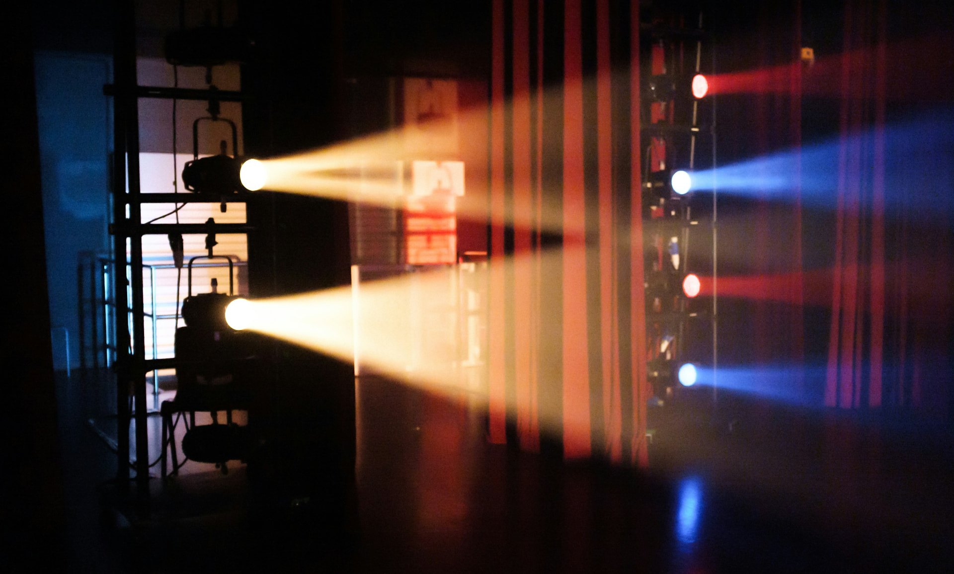 Fari di scena accesi in un teatro, con fasci di luce caldi, rossi e azzurri